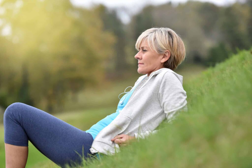 Older woman sitting on a hill outside.