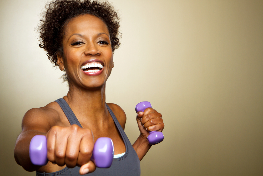 A happy, smiling woman holding small purple dumbbells for an upper body workout.