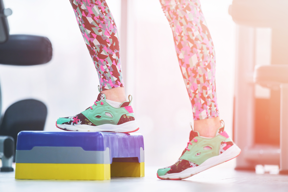 A woman's feet in colorful shoes stepping onto an aeriobics step platform.