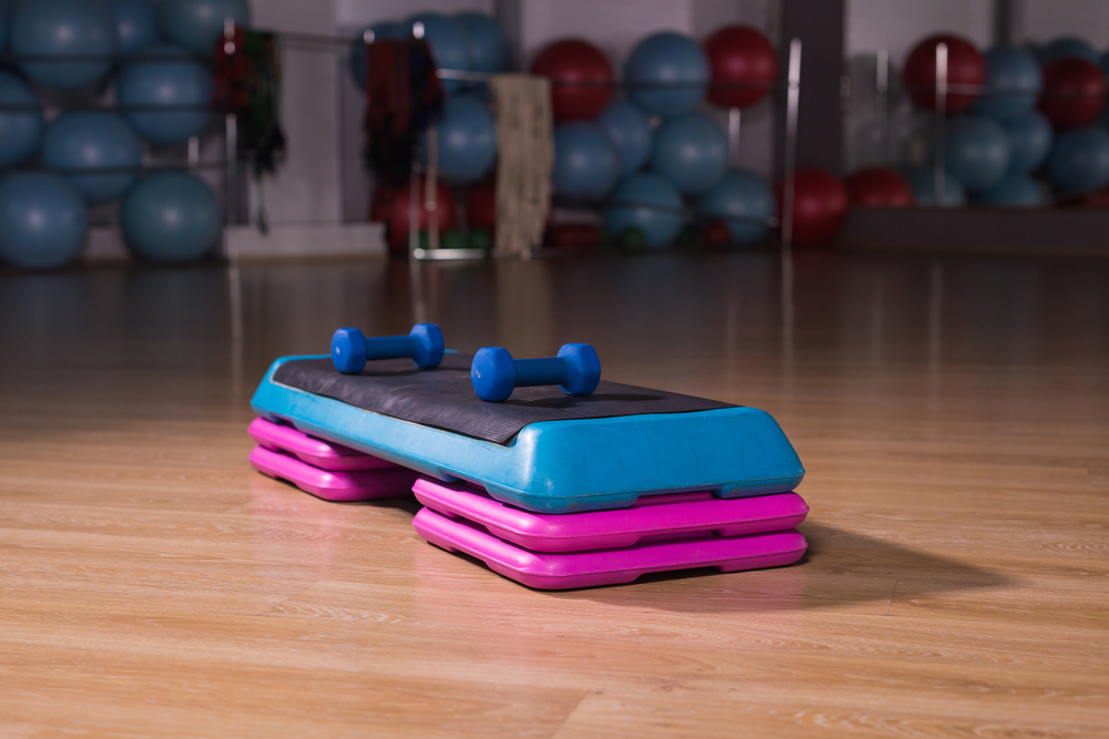 A bright pink and blue aerobics step platform with dumbbells set on top.