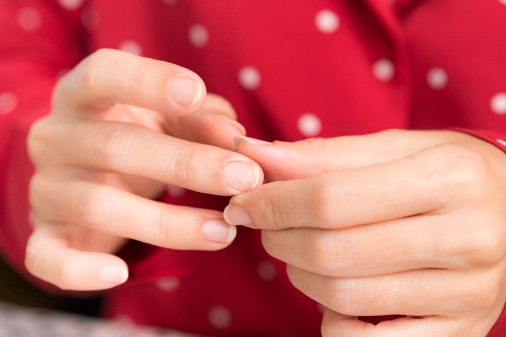 A woman looking at her brittle fingernails.